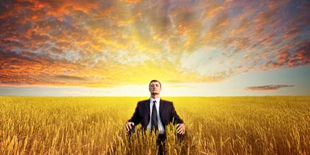 Picture of man meditating in business suite in the middle of a big field